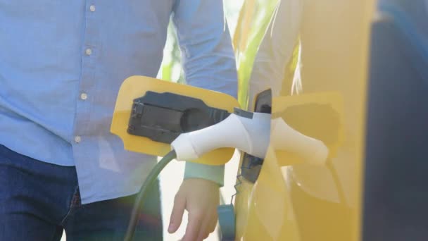 Tunnistamaton mies irrottaa latauskaapelin sähköauton. Miesten käsi katkaisee virtaliittimen EV-autoon — kuvapankkivideo