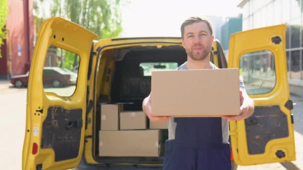 Portrait of a courier holding a parcel, a yellow car in the background. The courier delivers the parcel and hand it to the client — Video