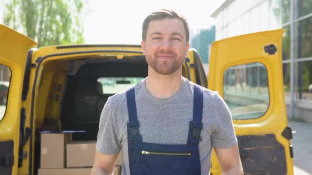 Portrait of a courier holding a parcel, a yellow car in the background. The courier delivers the parcel and hand it to the client — Vídeos de Stock