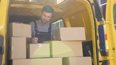 Delivery man writing something to clipboard. Courier checks the parcels