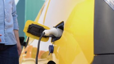 Tanımlanamayan adam kablolu elektrikli aracın fişini çekti. Erkek el, EV vagonuna güç bağlantısını kesiyor. Yeşil enerji kavramı