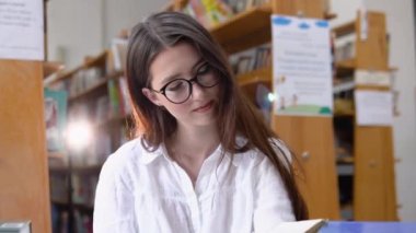 A thoughtful young student reads a book standing in the library