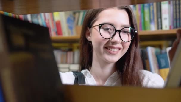 Κοντινό πλάνο ελκυστικό έφηβο κορίτσι ποζάρουν στη βιβλιοθήκη ματιά στην κάμερα. Φωτογραφία του φοιτητικού πορτραίτου των ιδρυμάτων τριτοβάθμιας εκπαίδευσης, εξαιρετική έννοια των σπουδών — Αρχείο Βίντεο