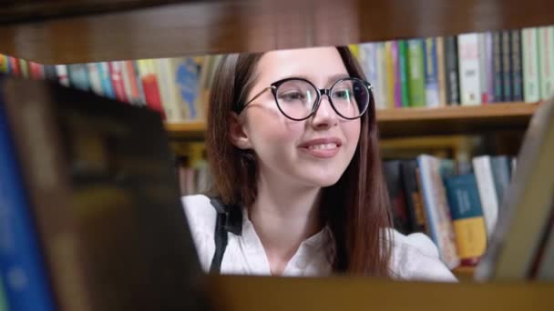 Een universiteitsstudent is op zoek naar een boek op boekenplanken in de bibliotheek — Stockvideo