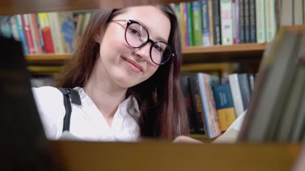 Close up attractive teenage girl posing in library look at camera. Head shot of higher education institution student portrait, excellent studies concept — Stock video