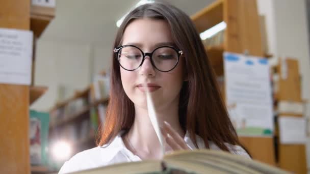 A thoughtful young student reads a book standing in the library — Video