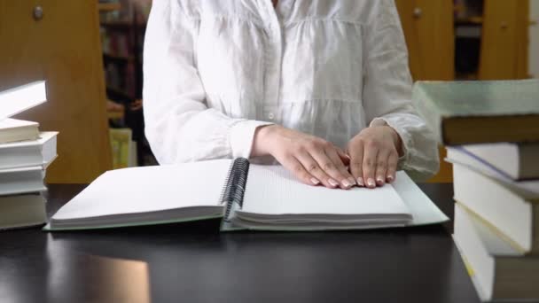 Female student studying in a library, sitting and reading a braille book — Stok video