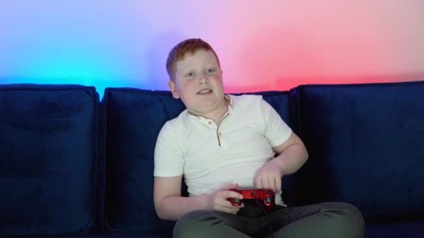 Excited little boy gamer is sitting on a couch, playing and winning in video games on console. Cozy room with warm and neon light