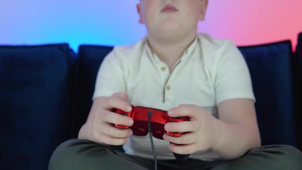 手放在一个控制器上玩电子游戏在一个黑暗的房间的电子竞技游戏比赛。兴奋的小男孩坐在沙发上，在游戏机上玩又赢 — 图库视频影像