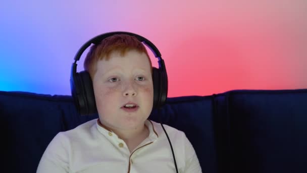 拍下了一个晚上在家里玩网络游戏的小男孩的肖像。游戏玩家在对着耳机说话时与队友讨论战术 — 图库视频影像