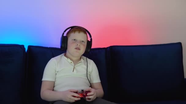 Gamer discussing tactics with teammates while talking into headset. Close up portrait of a little boy playing online computer video game in the evening at home — стоковое видео