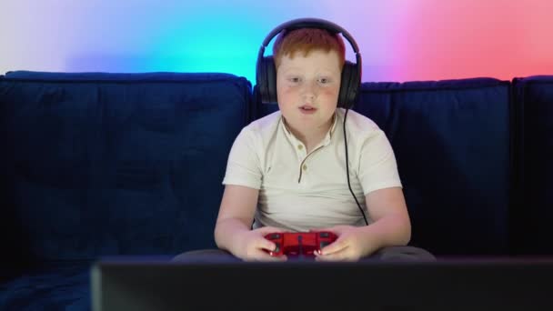 Gamer discussing tactics with teammates while talking into headset. A boy gamer is sitting on a couch, playing and winning in video games on console — Vídeo de stock