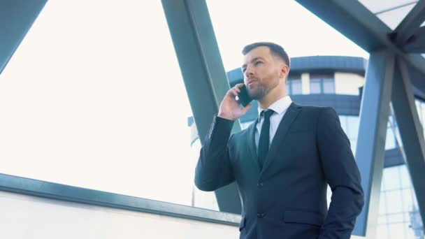 Empresário falando telefone celular perto de prédio de escritórios moderno. Retrato de homem de negócios feliz chamando telefone ao ar livre — Vídeo de Stock
