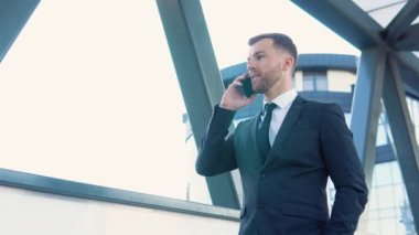 Modern ofis binasının yakınında konuşan bir iş adamı. Dışarıdaki telefonu arayan mutlu iş adamının portresi.