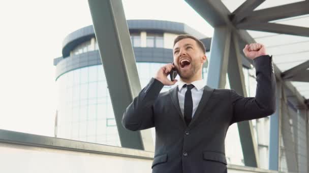 Excited overjoyed male winner celebrating success mobile phone victory. Portrait of happy business man calling phone outdoor — kuvapankkivideo