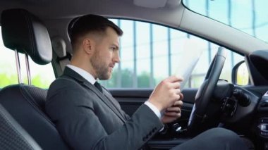 Kendine güvenen bir adamın portresi modern bir ofis binasının yanındaki iş elbisesiyle arabada oturuyor.