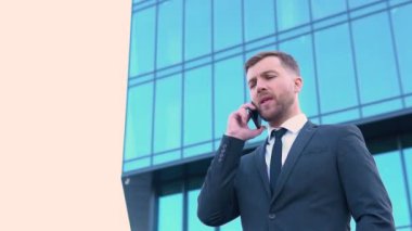 Dışarıdaki telefonu arayan mutlu iş adamının portresi. Modern ofis binasının yakınında konuşan bir iş adamı.