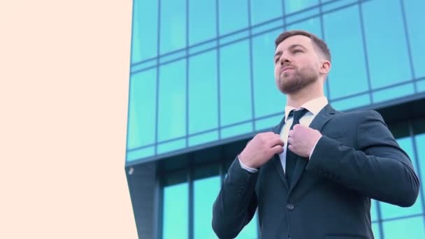 A well dressed happy bearded office corporate male executive standing outside a modern corporate building and adjusting suit and tie. Cityscape background — Vídeos de Stock