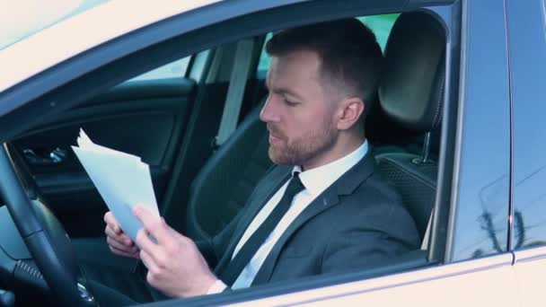 Portrait of a confident man sitting in a car with documents in a business suit near a modern office building — Vídeos de Stock
