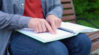 Genç kör bir adam parktaki bankta oturuyor ve kör alfabesiyle yazılmış bir kitap okuyor.