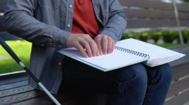 Genç kör bir adam parktaki bankta oturuyor ve kör alfabesiyle yazılmış bir kitap okuyor.