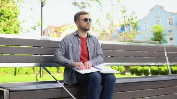 Hombre ciego leyendo el libro Braille, sentado en el banco en el parque de verano — Vídeo de stock