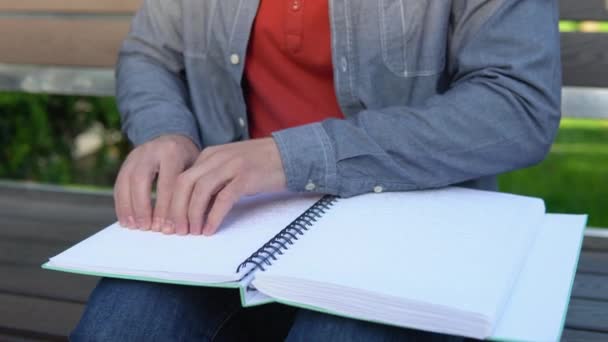 Blind man reading braille book, sitting on bench in summer park — Stock Video