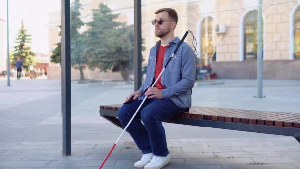 Joven ciego sentado en una parada de autobús — Vídeo de stock