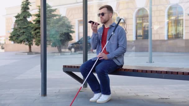 En blind man talar i telefon väntar på en buss vid en busshållplats — Stockvideo