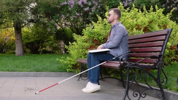 Blind man läser punktskrift bok, sitter på bänk i sommarparken — Stockvideo