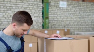 Teslimatçı adam panoya bir şeyler yazıyor. Kurye depodaki paketleri kontrol ediyor.