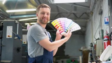 Renk paletli bir baskı fabrikasında çalışan bir mühendisin portresi. Baskı üretim sürecinde renk yönetimi kavramı. Yazdırma düzeltmesi için katalog örnekleri