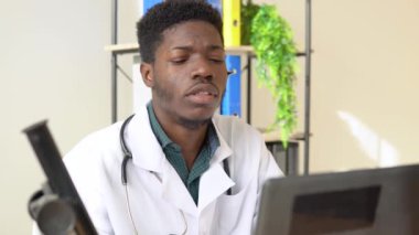 Kulaklık takmış genç Afrikalı Amerikalı erkek doktor laptopta sohbet ediyor ya da danışmanlık yapıyor.