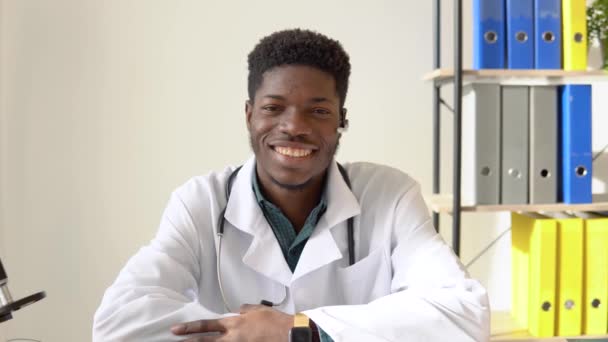 Young african american male doctor looking directly to the camera while sitting in hospital for online consultation — Stock Video