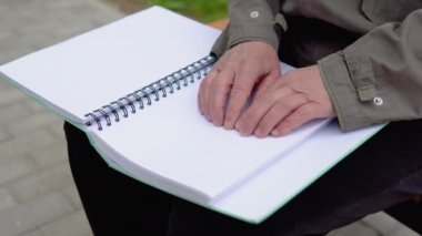 Şehir parkında bankta oturan kör bir adam kabartma kitap okuyor.