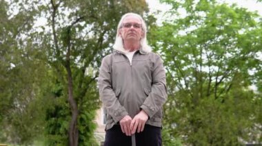 Elinde baston tutan kıdemli adam parkta duruyor.