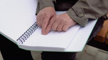 Şehir parkında bankta oturan kör bir adam kabartma kitap okuyor.