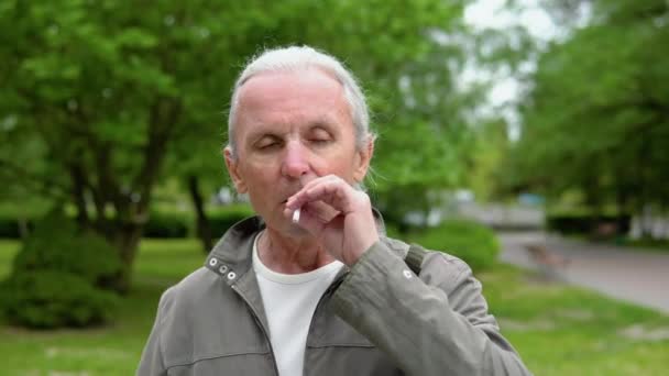 都市部の公園での喫煙中にカメラにポーズをとるしわ顔を持つスタイリッシュな老人の肖像画 — ストック動画