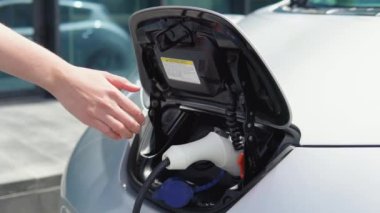 Elektrikli arabasının şarj aletini çıkartan bir kızın elini yakından görebilmek için.