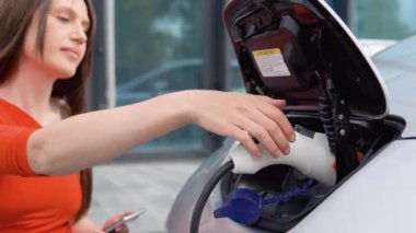 Elektrikli arabasının şarj aletini çıkartan bir kızın elini yakından görebilmek için.