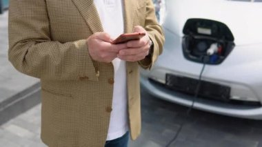 Üst düzey işadamı akıllı telefon kullanıyor ve elektrikli araçlara güç kaynağı bağlayıp arabadaki aküyü şarj ediyor. Şarj istasyonundan bir elektrikli arabayı şarj etmek