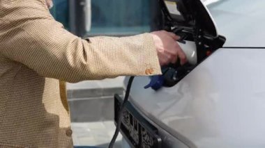 Tanımlanamayan yaşlı adam elektrikli araca kablo bağlıyor. Erkek aktif hale getirmek için telefon kullanıyor. Şarj istasyonundan bir elektrikli arabayı şarj etmek