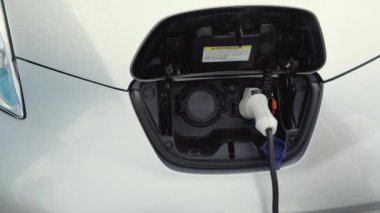 Tanımlanamayan yaşlı adam elektrik kablosunu elektrikli araca bağladı. Erkek el güç bağlantısını EV vagonuna bağlar ve pilleri şarj eder. Şarj istasyonundan bir elektrikli arabayı şarj etmek