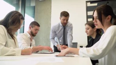 Bir grup genç erkek ve kadın ofis çalışanı bir konferans veya yönetim kurulu toplantısında bir proje üzerinde oturup tartışıyorlar.