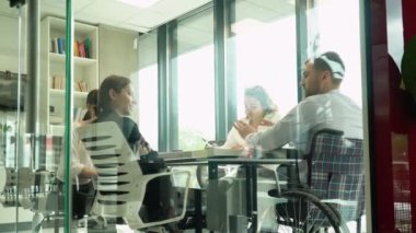 Bir grup iş arkadaşı ofis toplantısında konuşuyor, biri tekerlekli sandalyede. Modern bir ofiste bağımsız yaratıcı iş