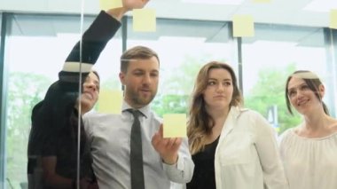 Genç şirket çalışanları ofiste çıkartmalarla bir iş planını tartışıyor.