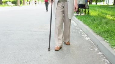 Parkta bastonla yürüyen yaşlı kadınların bacaklarını kapat. Parkta güneşli bir günün tadını çıkaran yaşlı bir kadın, emeklilik tatili.