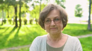 Parkta kameraya poz veren gülümseyen son sınıf öğrencisi kadın. Kıdemli bayan kameraya bakıyor. Yaşlı kadın kameradan başını çeviriyor. Kadın model dışarıda tek başına duruyor.