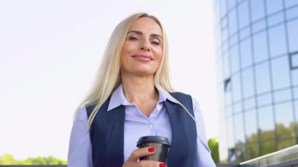 コーヒーカップ付きのモダンな企業ビルの外に立っているビジネスマンの女性 都市景観 — ストック動画