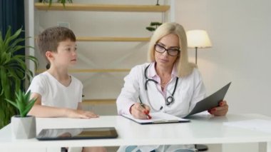 Üniformalı kıdemli kadın aile doktoru klinikteki check-up toplantısında küçük çocuk hastaya danışıyor. Arkadaş canlısı çocuk doktoru küçük çocuğa beşlik çakıyor ve iyi tedavi sonuçlarını kutluyor.
